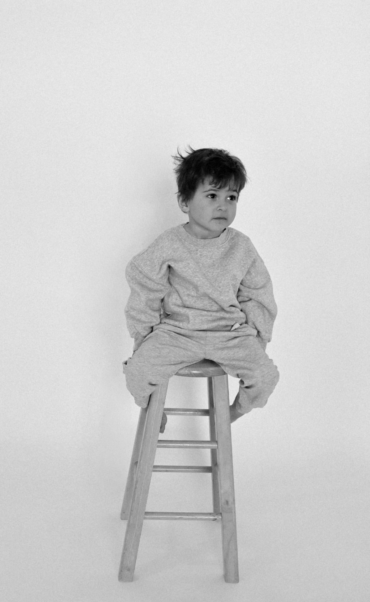 Black and white studio portrait of a boy sitting on a wooden stool