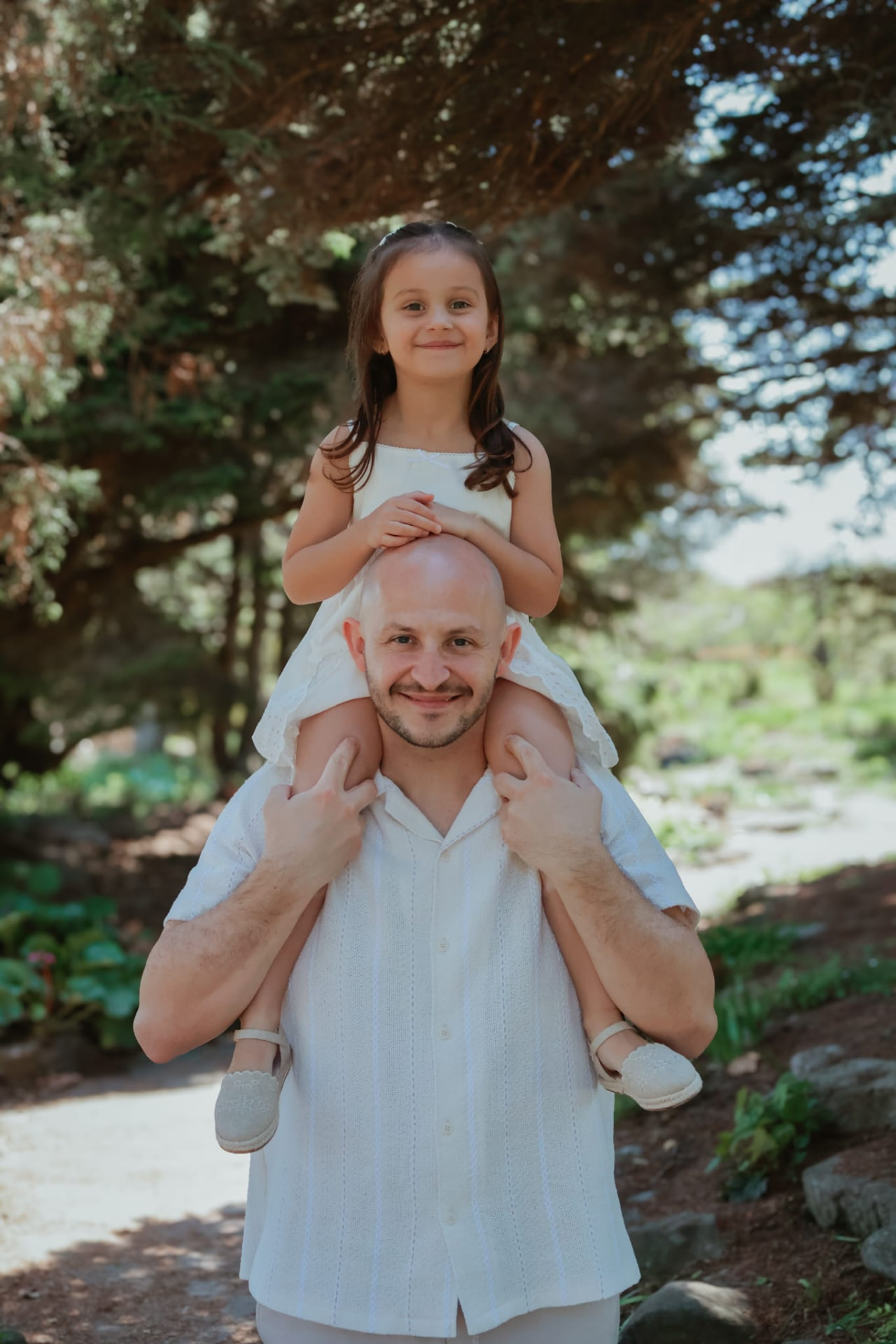 Father carrying his daughter on his shoulders under the trees