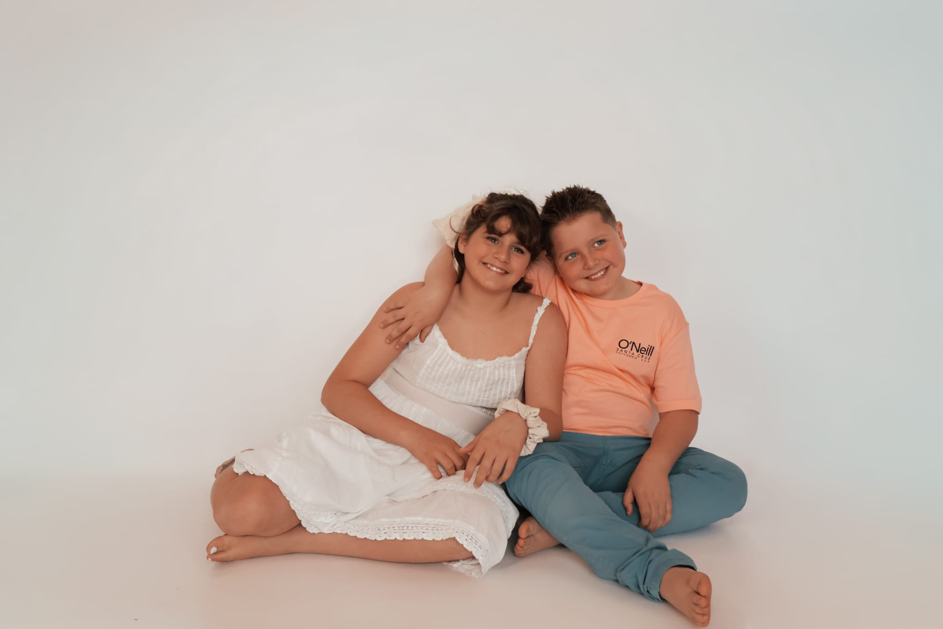 Brother and sister sitting together on a clean studio backdrop