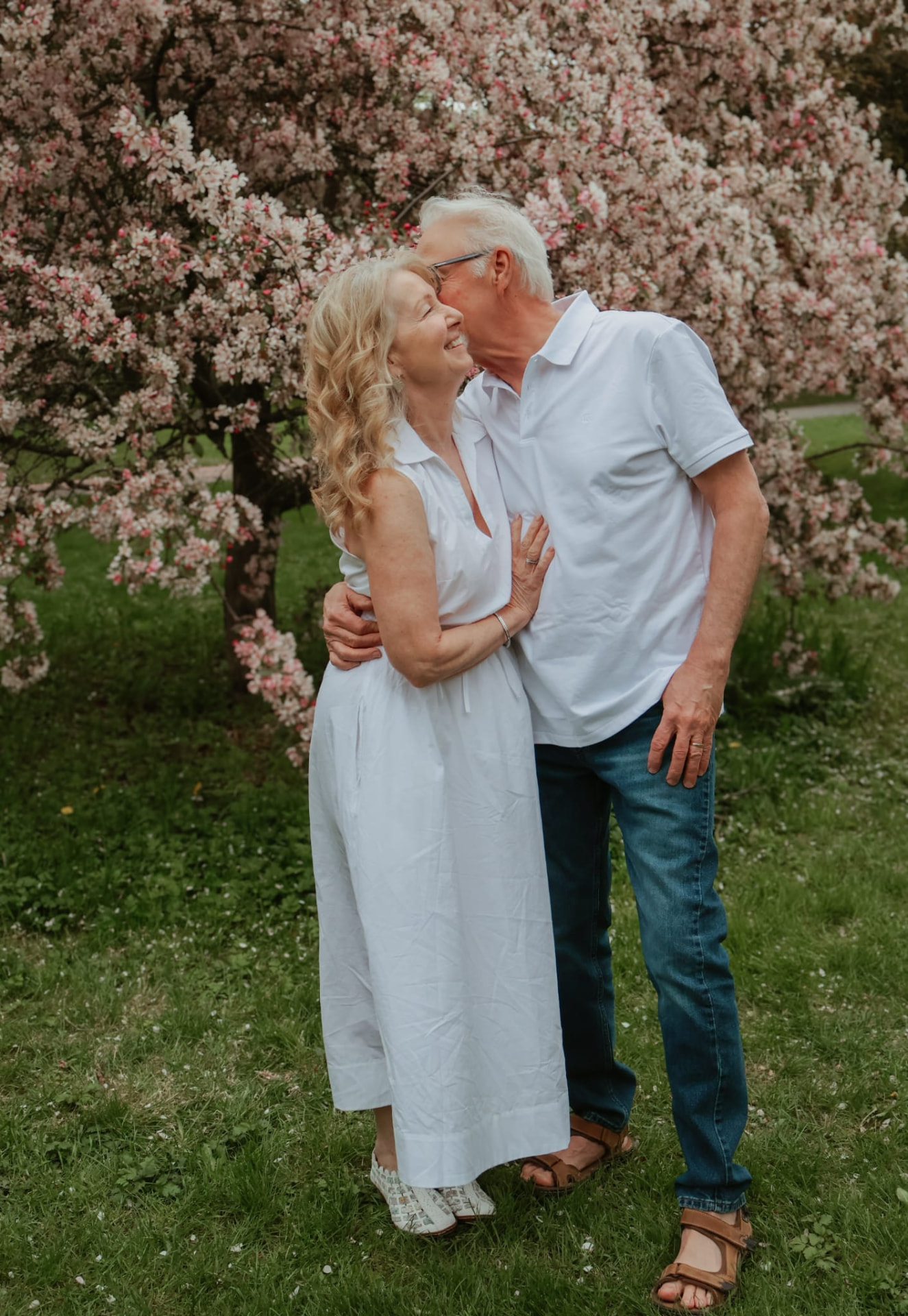 Older couple in white embracing beneath a blossoming tree