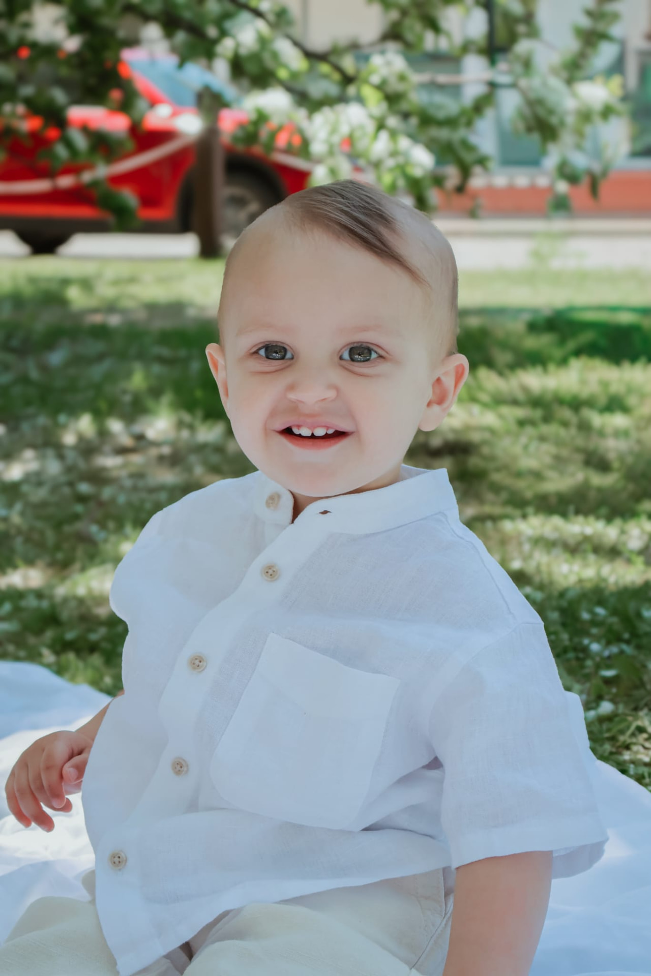 Toddler boy in a white linen shirt smiling on the grass